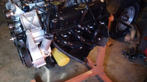 1993 Ford Bronco - Engine assembly on an orange stand, a yellow oil filter and black exhaust manifolds, with a tire visible in the background.