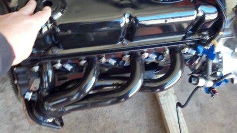 1993 Ford Bronco - Ford engine with shiny exhaust headers and a hand reaching for a component.