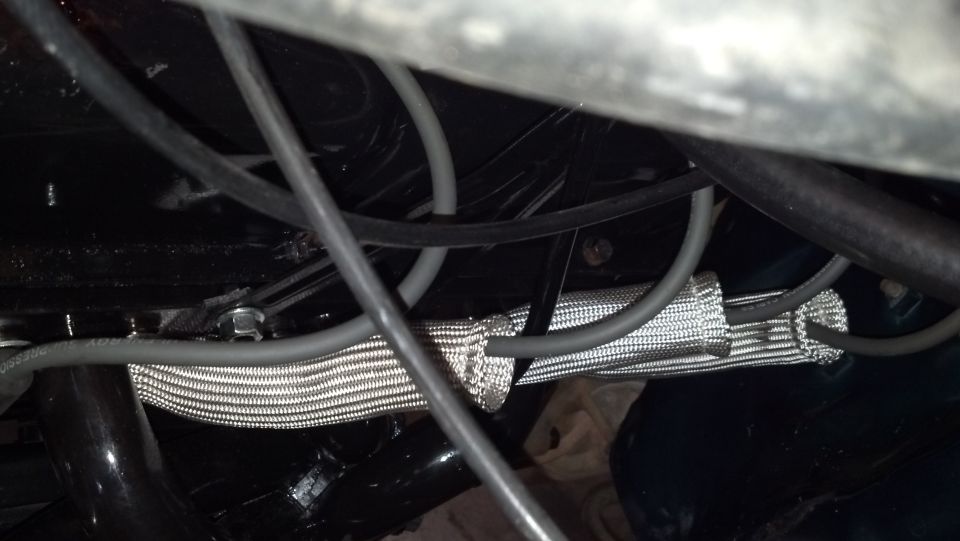 Close-up of engine bay wiring and a silver heat shield protecting a hose