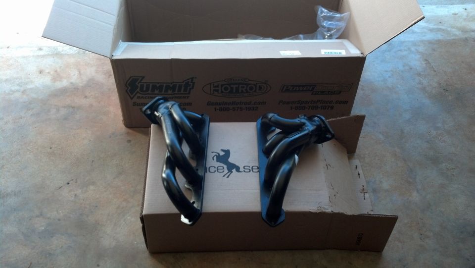 Two black exhaust headers sitting on cardboard boxes, one box open