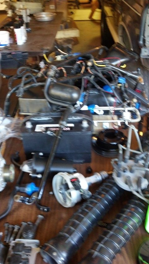 1993 Ford Bronco - Various automotive parts are spread across a wooden surface, including a battery and engine components.