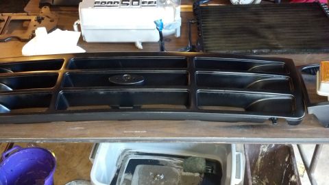 1993 Ford Bronco - A black grille, likely from a Ford truck, is shown on a workbench with other automotive parts.
