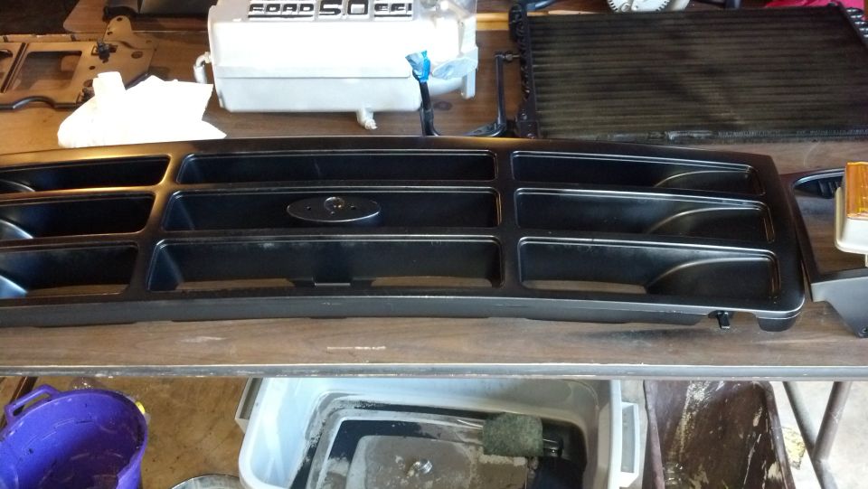 Black grille with Ford oval emblem, sitting on a workbench next to a radiator
