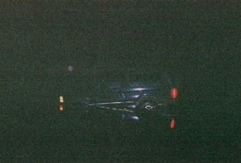 1995 Ford Bronco - A dark vehicle is seen from the rear, with its red taillights illuminated against a dark background.