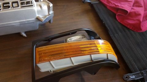 1993 Ford Bronco - A disassembled Ford Bronco turn signal assembly and engine part are laid out on a wooden surface.
