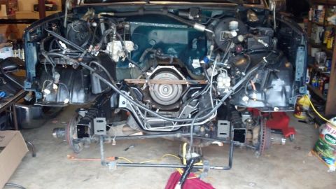 1993 Ford Bronco - The front end of a vehicle is disassembled in a garage, showing the engine and transmission area with the transmission removed and suspensi…