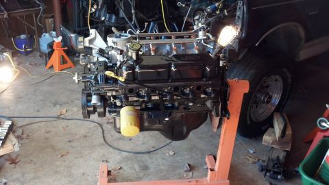 1993 Ford Bronco - Engine assembly is out of the vehicle and on a stand for work, with a tire and part of the fender visible.