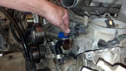 1993 Ford Bronco - Close-up view of a hand disconnecting a sensor within a vehicle's engine compartment, surrounded by various mechanical components.