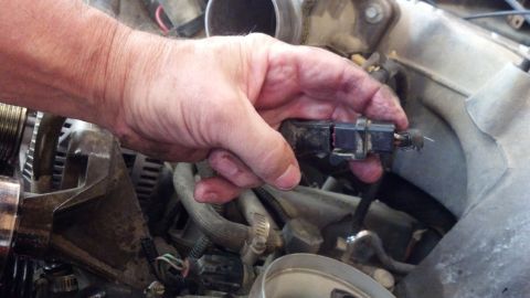 1993 Ford Bronco - Close-up of a hand disconnecting a sensor from an engine component.