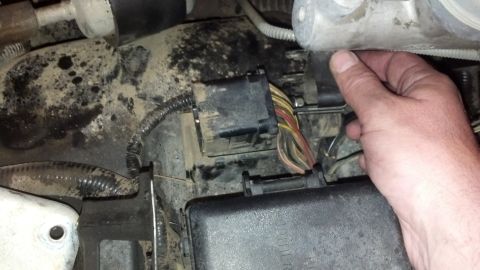 1993 Ford Bronco - A hand reaches for a connector in a messy engine compartment, showing various wires and components.