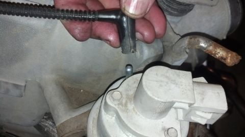 1993 Ford Bronco - A close-up view of an engine component with a vacuum hose disconnected and a corroded metal tube nearby.