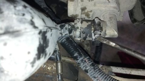 1993 Ford Bronco - A close-up view of a dirty engine part, possibly during a tear-down, with a screwdriver engaged.