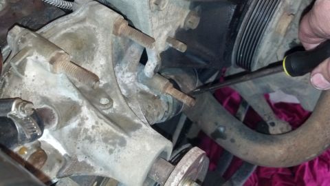 1993 Ford Bronco - A hand uses a screwdriver to work on a vehicle's engine water pump assembly.
