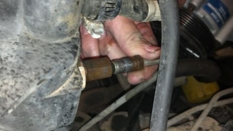 1993 Ford Bronco - A mechanic's hand tightens a metal fitting within a vehicle's engine compartment.