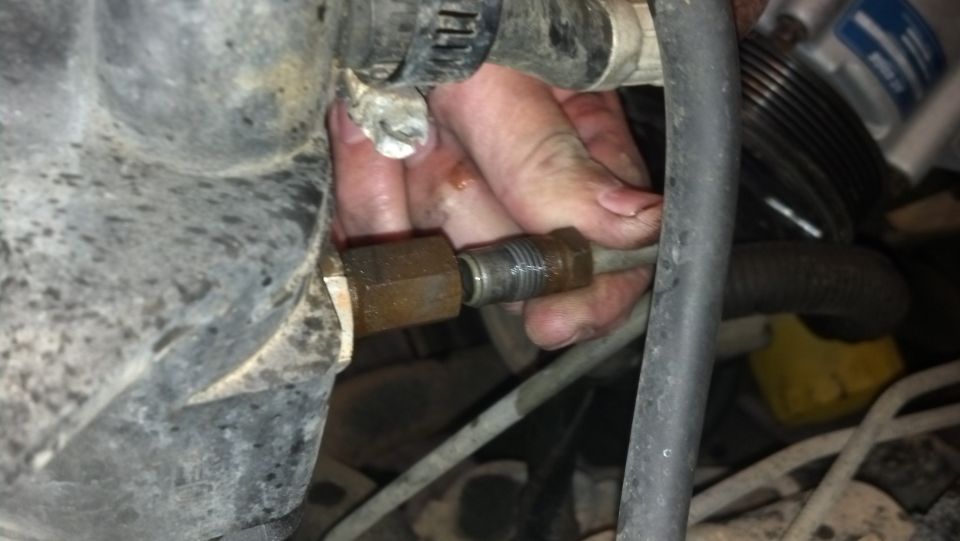 Close-up of a hand working on a metal fitting in an engine bay
