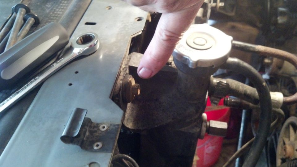 hand pointing at radiator cap and hoses, wrench and screwdriver nearby