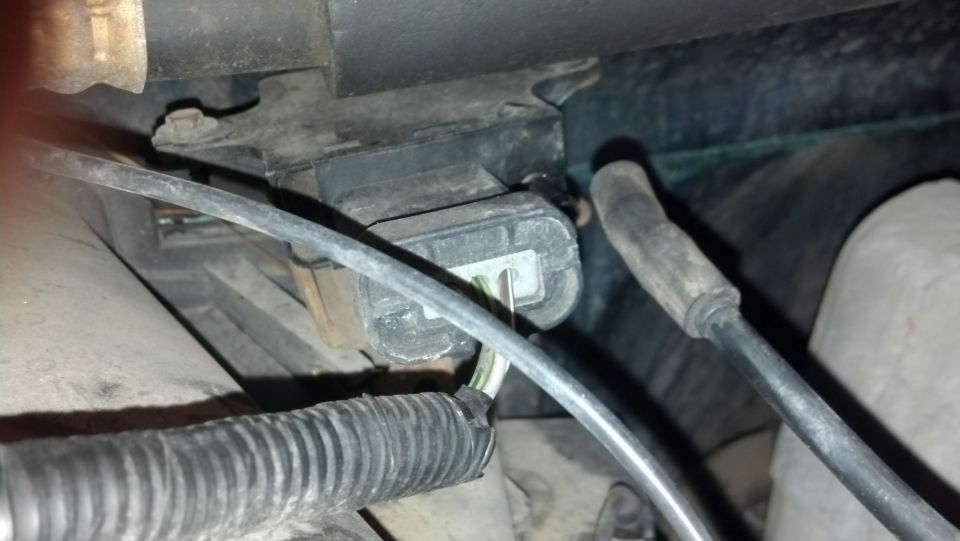 Close-up of a black electrical connector with wires attached, part of a vehicle's engine bay