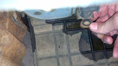 1993 Ford Bronco - A hand holds a small metal part over a wet, gridded surface, likely during a vehicle tear-down or repair.