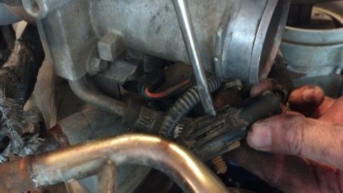 1993 Ford Bronco - A close-up view of engine components, showing a hand disconnecting a wire harness.