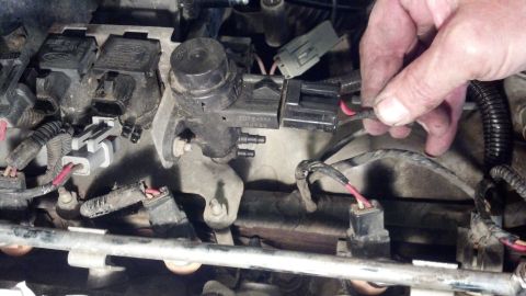 1993 Ford Bronco - A hand disconnects a wire from a sensor on an engine. The part has text that reads FOTB-AMA.