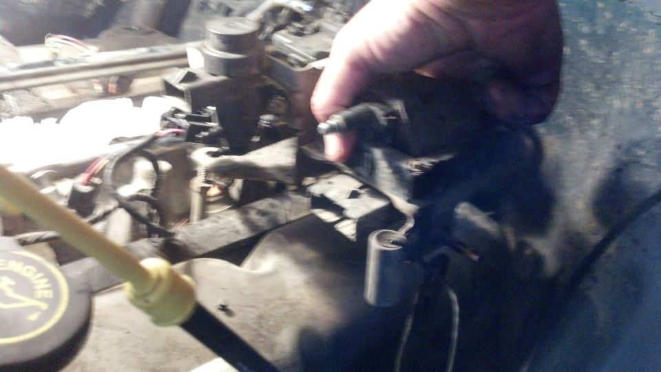Engine bay with a hand reaching for a component. A yellow dipstick is visible