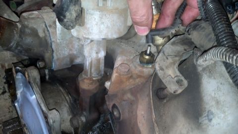1993 Ford Bronco - A hand disconnects a sensor from an engine component, likely during a tear-down process.