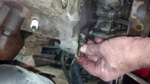 1993 Ford Bronco - Mechanic's hand removing a bolt from an engine block, with a spark plug visible.