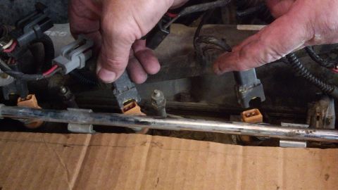 1993 Ford Bronco - Hands disconnect fuel injectors from a vehicle's fuel rail.