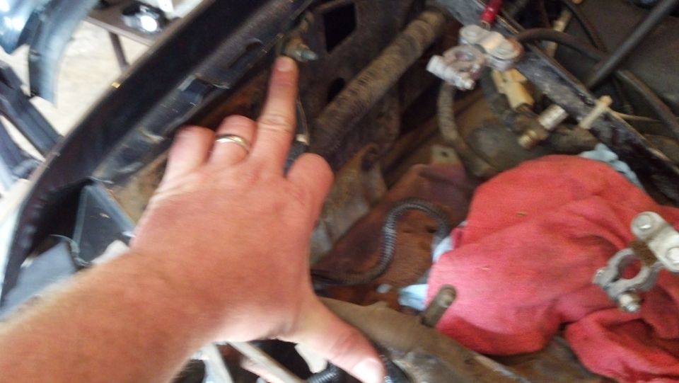 Engine bay with a hand pointing to hoses and wires. Red cloth is visible