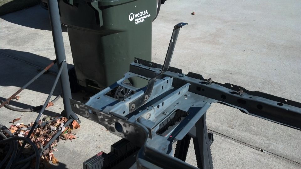 Vehicle frame section on a stand, with a trash can in the background