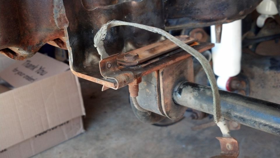 Rusty rear axle assembly with a white shock absorber and a grounding strap