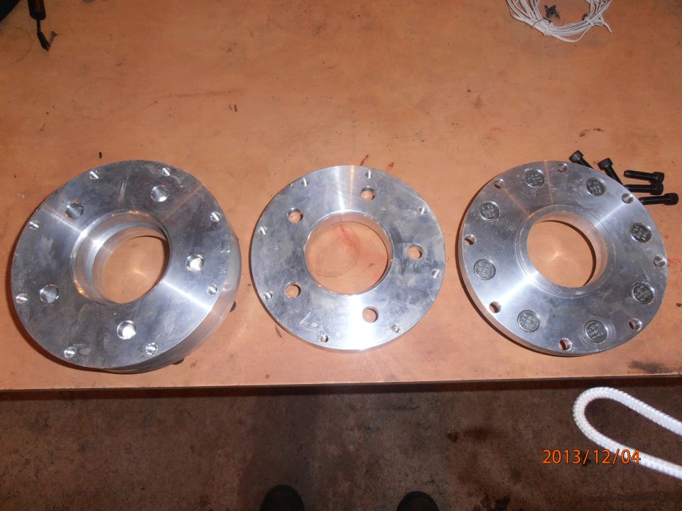 three metal wheel spacers with bolt holes on a wooden surface