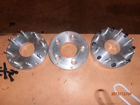 1996 Ford Bronco - Three metal wheel spacers with bolts are laid out on a wooden surface.