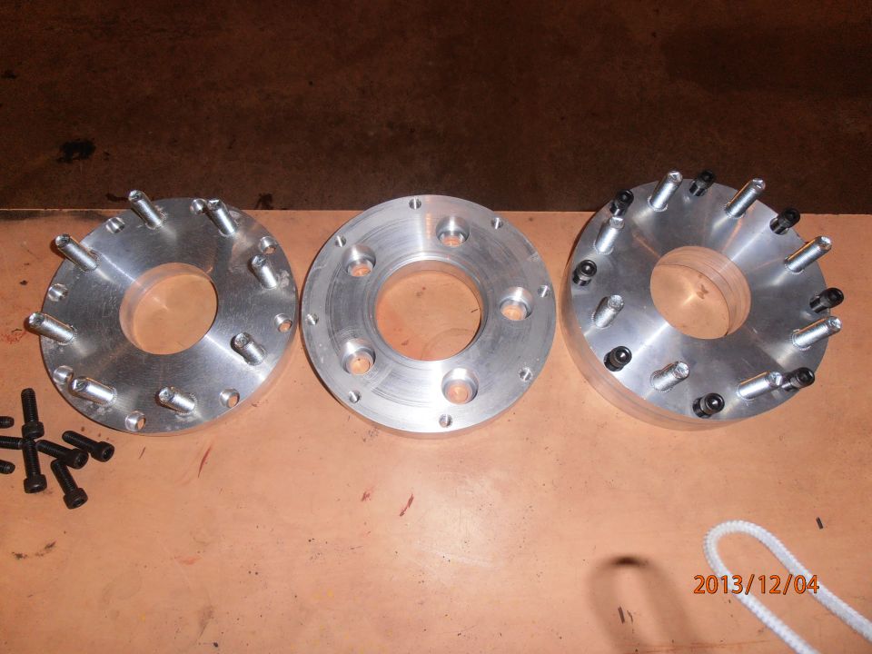 Three metal wheel spacers with bolts on a wooden surface