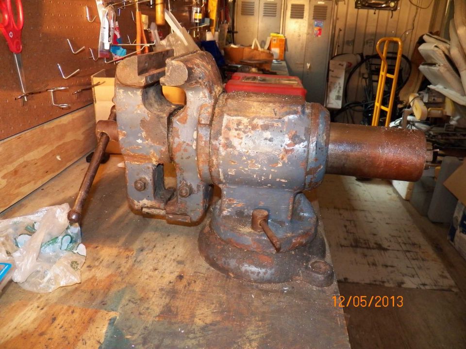 Rusted gray bench vise with red accents on a wooden workbench, showing wear and tear