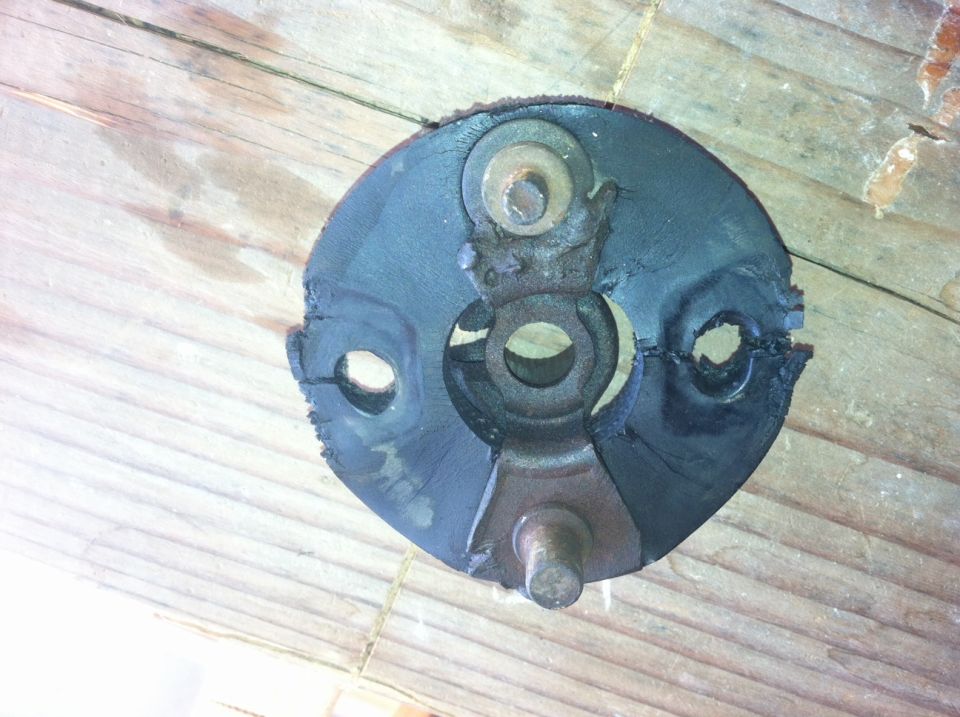 Close-up of a damaged rubber and metal component, possibly a motor mount or U-joint bearing, resting on a wooden surface