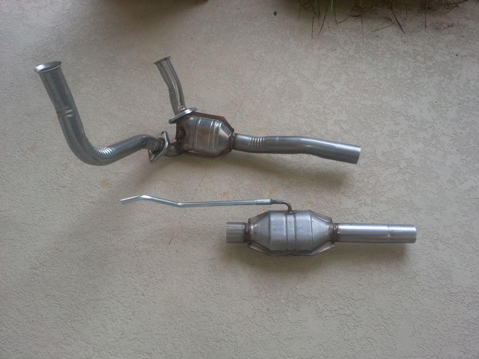 Two catalytic converters and exhaust pipes laid out on a concrete surface