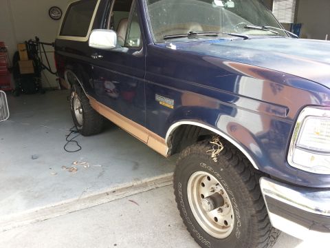 1994 Ford Bronco - A blue Ford Bronco with tan trim is parked in a garage, showing its side and front quarter panel.