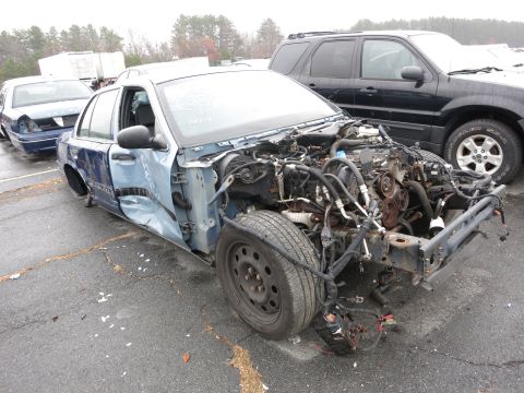 1991 Ford LTD Crown Victoria - A damaged blue sedan sits in a lot, its engine compartment exposed to the elements.