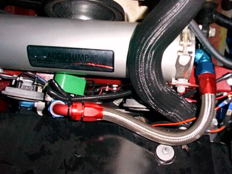 1967 Ford 427 - Close-up of an accusump oil accumulator with braided hoses and fittings attached.
