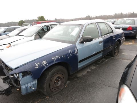 1991 Ford LTD Crown Victoria - A damaged Ford Crown Victoria sits in a junkyard with other vehicles.