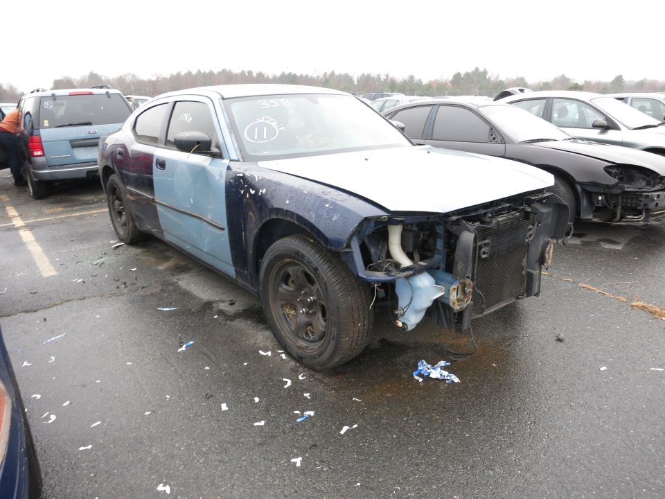 Damaged Dodge Charger with mismatched blue and dark blue panels, missing front end parts. Another car is parked behind it
