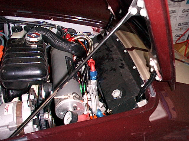 Air-conditioning components, canister and hoses under the raised hood of a maroon car