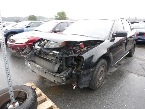 1991 Ford LTD Crown Victoria - A damaged black sedan sits in a junkyard with its hood open and front bumper missing.