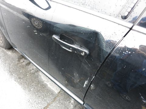 1991 Ford LTD Crown Victoria - Close-up of a black car door showing a dented section near the handle and numerous scratches on the surface.