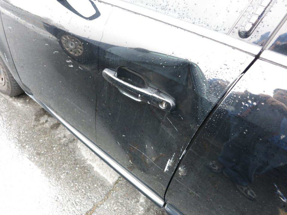 Black car door with chrome handle, dent, and scratches