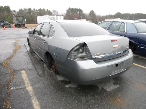 1991 Ford LTD Crown Victoria - Silver sedan with significant rear damage, missing one taillight and wheel, parked outdoors.
