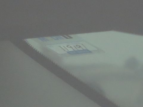 1991 Ford LTD Crown Victoria - Low-quality, washed-out photo of a VIN/data plate seen through a windshield with partial numbers visible.
