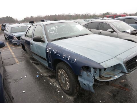 1991 Ford LTD Crown Victoria - A two-tone sedan, possibly a Ford Crown Victoria, sits in a junkyard with its front end damaged and missing headlights.