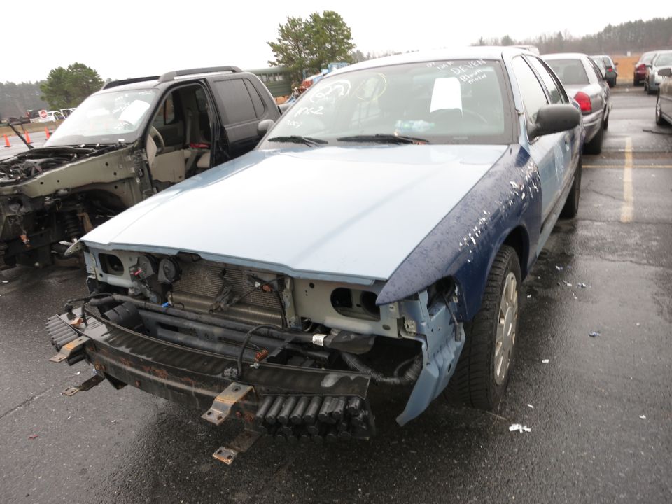 Front view of a wrecked 1991 Ford Crown Victoria LTD with its bumper and grille removed, parked next to another damaged SUV